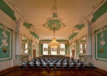 305 - Ratzeburg - Kreismuseum Rokkokosaal.jpg Im Rokokosaal des Kreismuseums stehen viele Stühle, Wände und Decke haben Stuck mit Farben, in der Mitte hängt ein Kronleuchter