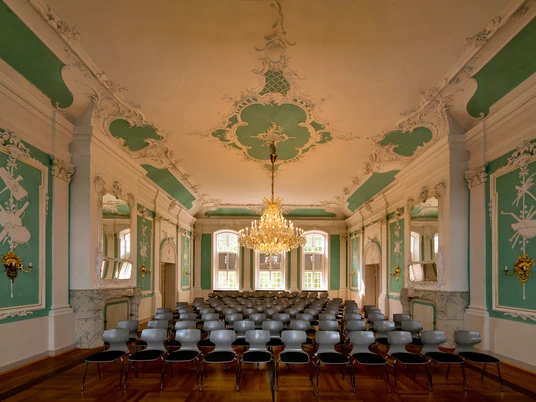 305 - Ratzeburg - Kreismuseum Rokkokosaal.jpg Im Rokokosaal des Kreismuseums stehen viele Stühle, Wände und Decke haben Stuck mit Farben, in der Mitte hängt ein Kronleuchter