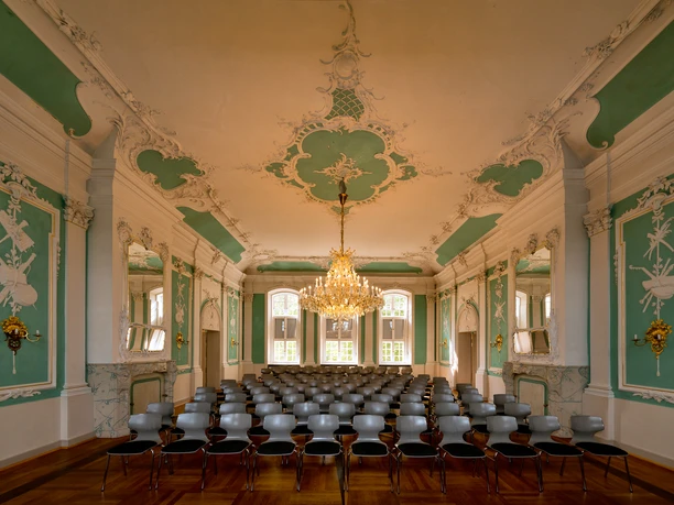 305 - Ratzeburg - Kreismuseum Rokkokosaal.jpg Im Rokokosaal des Kreismuseums stehen viele Stühle, Wände und Decke haben Stuck mit Farben, in der Mitte hängt ein Kronleuchter