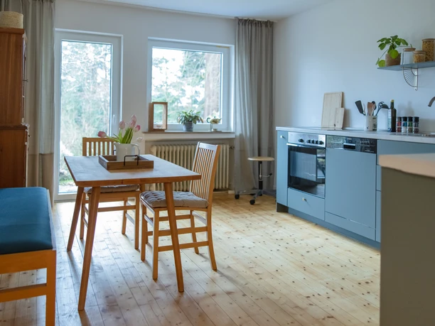 Waldferienwohnung_Küche_Katharina_Hein.jpg Gemütliche Küche mit Holzboden, Essbereich mit Tisch und Stühlen, angrenzend großes Fenster.