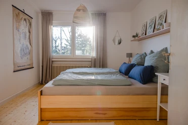 Waldferienwohnung_Schlafzimmer_Katharina_Hein.JPG Helles Schlafzimmer mit Holzboden, einem großen Doppelbett mit blauen Kissen und einem Fensterblick ins Grüne.