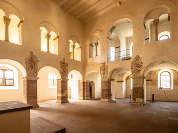 Lichtdurchfluteter romanischer Kircheninnenraum mit hohen Bögen und dekorativen Säulenstrukturen.