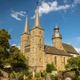 Stiftskirche St. Bonifatius in einer grünen Umgebung mit zwei Türmen, klarem Himmel im Sommer.
