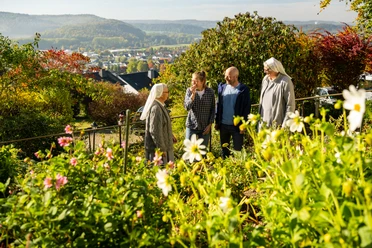 Warburg-Scherfede-Zionsberg-Teutoburger-Wald-Tourismus-D-Ketz-042.jpg Blühender Garten mit vier Personen im Gespräch, darunter zwei Nonnen, umgeben von herbstlicher Landschaft.
