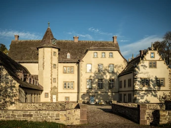 Historisches Schloss mit Natursteinmauern, runden Türmen und einem Innenhof bei sonnigem Wetter.