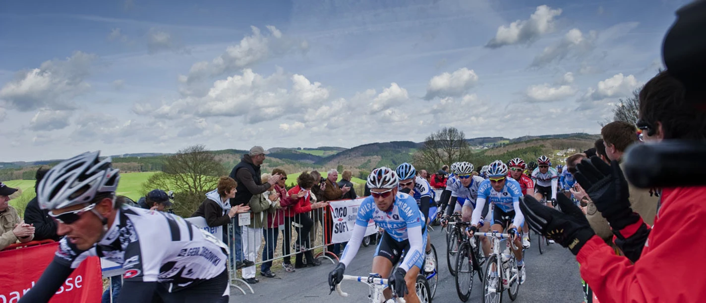 Rund um Köln Radfahrer in einem Rennen auf ländlicher Straße, mit jubelndem Publikum am Straßenrand.