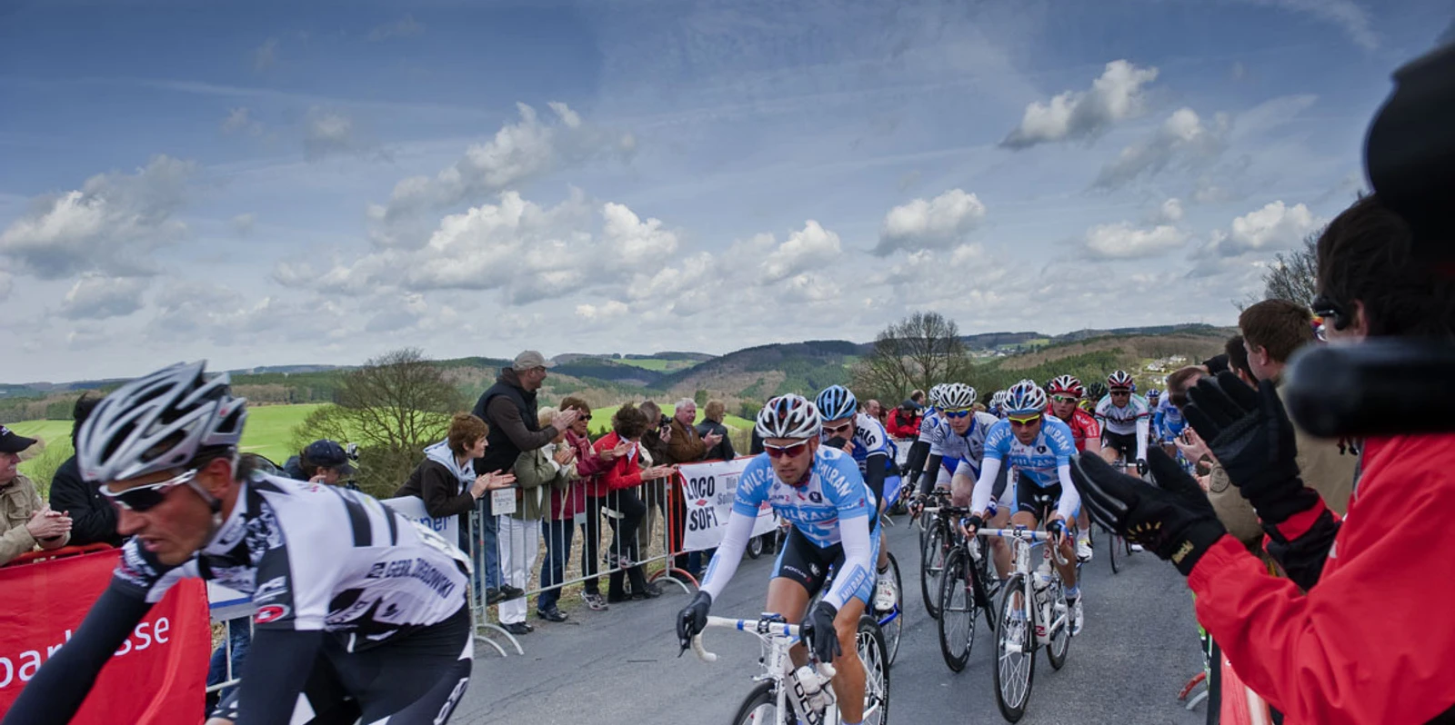 Rund um Köln Radfahrer in einem Rennen auf ländlicher Straße, mit jubelndem Publikum am Straßenrand.