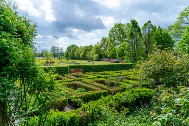 Garten_Privatgarten_Kneipp_Gertje-17.jpg Ein wunderschöner Garten mit grünen Hecken, einer Bank und blühenden Sträuchern.