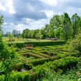 Garten_Privatgarten_Kneipp_Gertje-17.jpg Ein wunderschöner Garten mit grünen Hecken, einer Bank und blühenden Sträuchern.