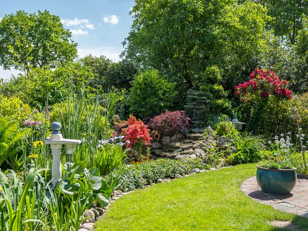 Garten_Privatgarten_Mueller Bollenhagen-1.jpg Ein idyllischer Garten mit verschiedenen Pflanzen in sattem Grün, bunten Blumen und einem kleinen Teich.
