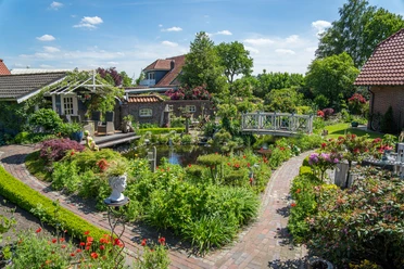 Garten_Privatgarten_Mueller Bollenhagen-32.jpg Ein idyllischer Garten mit blühenden Blumen, einem Teich und einer weißen Brücke.