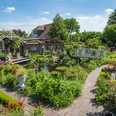 Garten_Privatgarten_Mueller Bollenhagen-32.jpg Ein idyllischer Garten mit blühenden Blumen, einem Teich und einer weißen Brücke.