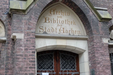 Tür in einem steinernen Torbogen, in den in alter Schrift "Archiv und Bibliothek der Stadt Aachen" eingemeißelt ist.