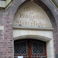 Tür in einem steinernen Torbogen, in den in alter Schrift "Archiv und Bibliothek der Stadt Aachen" eingemeißelt ist.