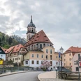 Stadtkirche Königstein Straßenszene mit Fachwerkhäusern und einer Kirche mit Turm, umgeben von Hügeln und bewölktem Himmel; frühlingshafte Atmosphäre.