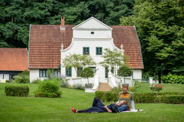 Im Künstlerdorf Worpswede Twee mensen ontspannen op een grasveld voor een wit historisch huis in Worpswede.