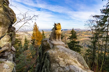 Katzfels Stenen lynxbeeld op een rots met uitzicht op een herfstbos en blauwe lucht op de achtergrond.