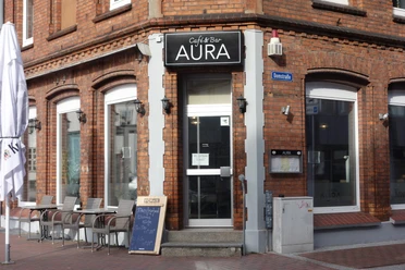 Café BarAura - Bernadette Raffenberg 09.03.23.jpg Rotes Haus mit Sitzplätzen davor und einem Schild mit der Aufschrift „Aura“