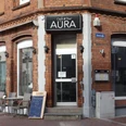 Café BarAura - Bernadette Raffenberg 09.03.23.jpg Rotes Haus mit Sitzplätzen davor und einem Schild mit der Aufschrift „Aura“