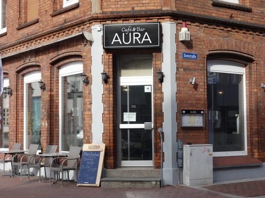 Café BarAura - Bernadette Raffenberg 09.03.23.jpg Rotes Haus mit Sitzplätzen davor und einem Schild mit der Aufschrift „Aura“
