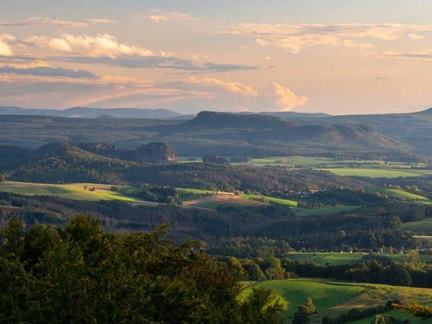 Pohled z Ungerbergu Rozlehlá krajina s kopci a lesy ve večerním světle, pod oblohou s pastelově zbarvenými mraky.