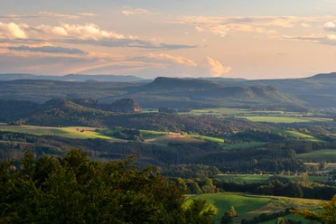 View from Ungerberg Vast landscape with rolling hills and forests in the evening light, under a sky with pastel-colored clouds.