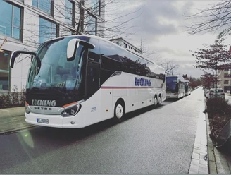 Ausflugsfahrt Lücking Busreisen Zwei moderne Reisebusse der Firma Lücking auf einer städtischen Straße, umgeben von Gebäuden.