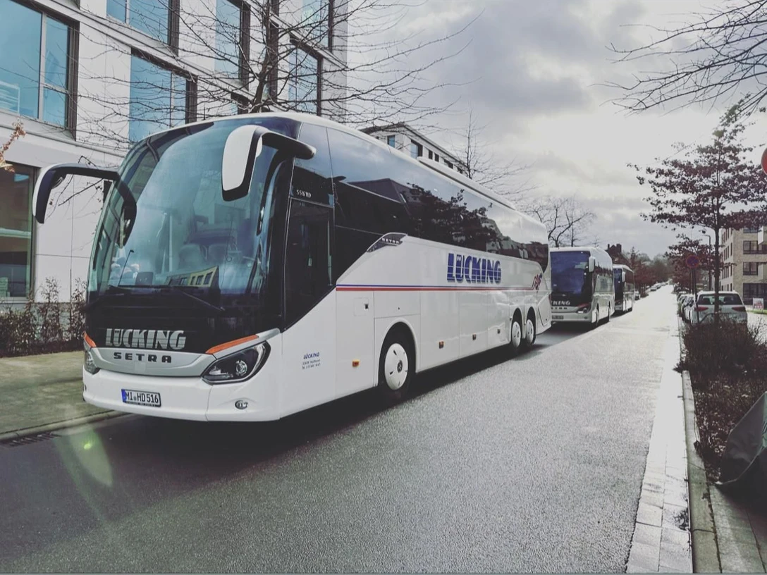 Ausflugsfahrt Lücking Busreisen Zwei moderne Reisebusse der Firma Lücking auf einer städtischen Straße, umgeben von Gebäuden.