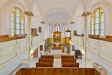 Radfahrerkirche Stadt Wehlen Innenansicht einer Kirche mit weißen Wänden, bunten Glasfenstern, Holzbänken und einem Altar mit Gemälde. Helle, ruhige Atmosphäre.