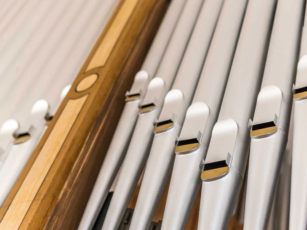 Orgel der Radfahrerkirche Close-up of silver organ pipes with golden details, flanked by a wooden frame with decorative patterns.