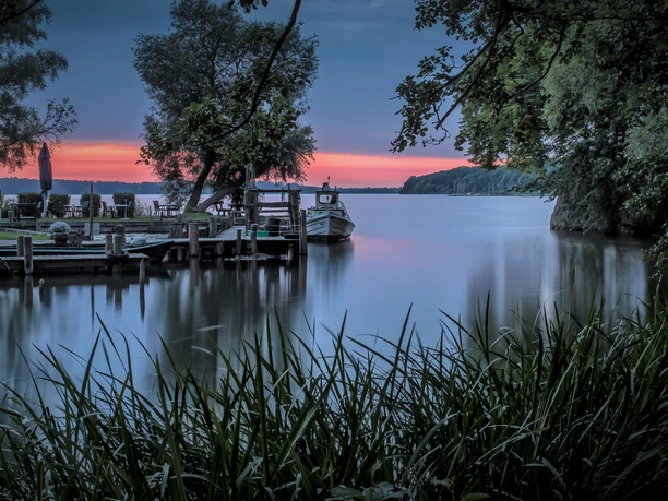 Sonnenuntergang Ratzeburger See.jpg Der Ratzeburger See bei Sonnenuntergang. Am Ufer ist ein Steg mit Booten.