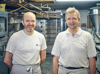Bäckerei Krätz Zwei Bäcker in weißer Kleidung stehen in einer Backstube.