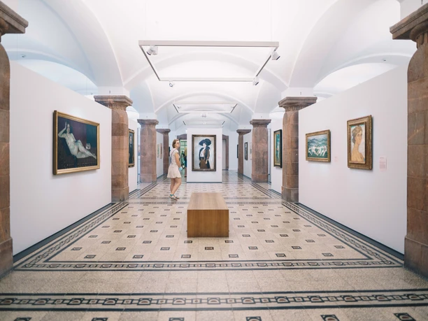 Kunstsammlungen_(c)Ernesto Uhlmann.jpg Besucher betrachtet Gemälde in einer Kunstgalerie mit elegantem Bodenmuster und Säulen.