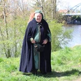Stadtführer Nienburg Eine mittelalterlich gekleidete Person steht vor einem Fluss, hinter einer modernen Brücke.