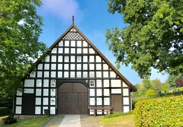 Heimathaus Wehdem Historisches Fachwerkhaus mit symmetrischem Design, umgeben von Bäumen und gepflegtem Rasen.