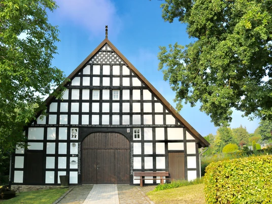 Heimathaus Wehdem Historisches Fachwerkhaus mit symmetrischem Design, umgeben von Bäumen und gepflegtem Rasen.