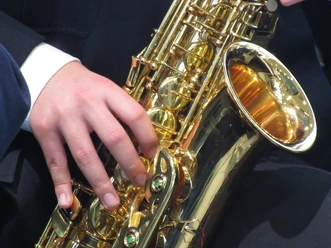 Saxophone Nahaufnahme eines glänzenden Saxophons in goldener Farbe, das von einer Person in dunkler Kleidung gespielt wird.