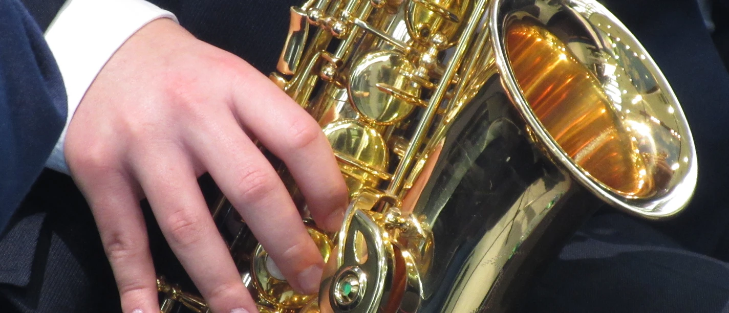 Saxophone Nahaufnahme eines glänzenden Saxophons in goldener Farbe, das von einer Person in dunkler Kleidung gespielt wird.