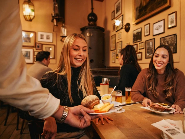 Früh im Veedel A waiter serves a woman a plate of Röggelchen (a type of bread) and a thick slice of cheese