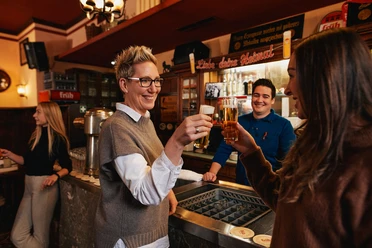 Früh im Veedel Scene in a rustic brewery: two women toast with Kölsch beer.