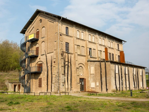 Historisches Backsteingebäude der Gedenkstätte Augustaschacht, umgeben von Bäumen und offener Wiese.