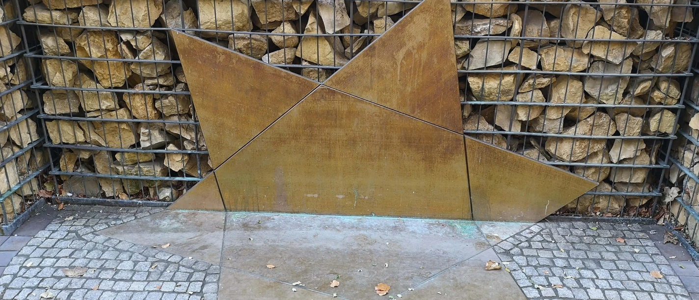 Zerbrochener Davidstern als Symbol für das zerstörte jüdische Leben Ein zerbrochener Davidstern auf Kies; Symbol für zerstörtes jüdisches Leben vor einer Steinwand.
