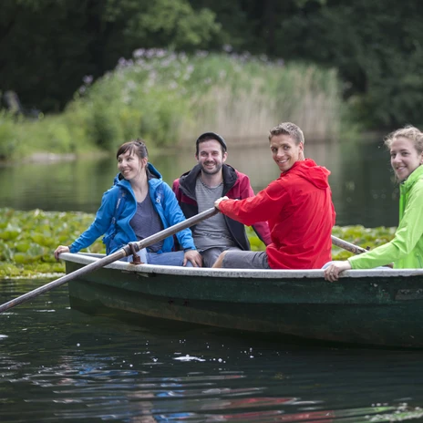 Boat trip with friends on Lake Albrechtshain - excursions in the Leipzig region Four friends paddling in a boat on Lake Albrechtshain, reeds in the background.