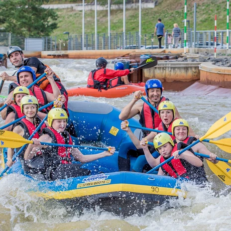 People in safety gear enjoy rafting on a challenging whitewater channel.