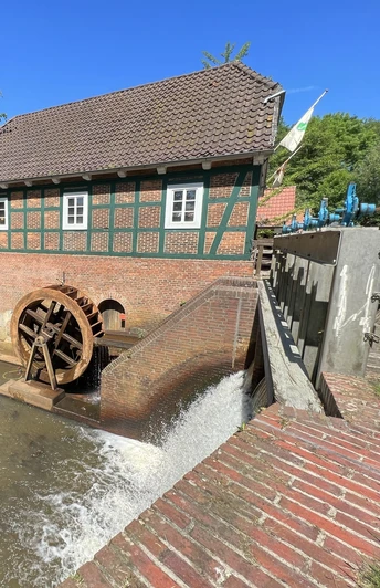 Mühlenrad der Wassermühle Meyenburg mit Bach und Mühlengebäude.Mill wheel of the Meyenburg watermill with stream and mill building.Møllehjulet på vandmøllen i Meyenburg med vandløb og møllebygning.Molenrad van de Meyenburg watermolen met beek en molengebouw.