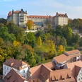 Pirna Schloss Sonnenstein Schloss Sonnenstein auf einem bewaldeten Hügel mit herbstlich gefärbten Bäumen, im Vordergrund rote Ziegeldächer und historische Gebäude.