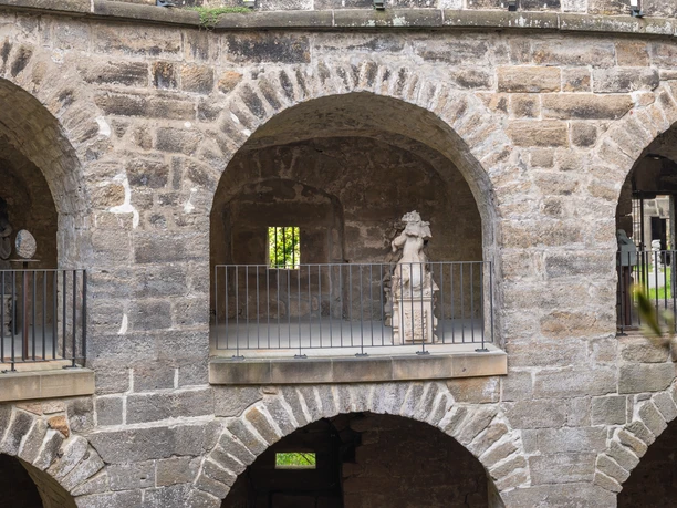 Schloss Sonnenstein Ausstellung Skulpturensommer Vorderansicht von Schloss Sonnenstein mit Steinbögen und Skulpturen, umgeben von Natur.