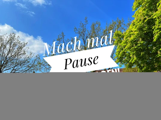 Mach mal Pause in Petershagen.jpg Blauer Himmel mit Bäumen und dem Schriftzug "Mach mal Pause" auf einem Banner in Petershagen.