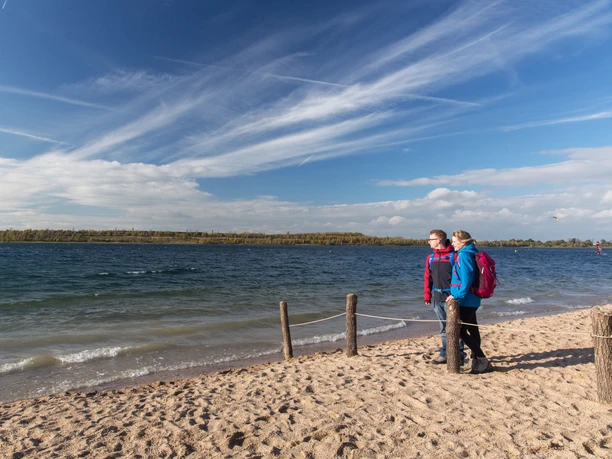 Para stoi na plaży jeziora Schladitz i patrzy na jezioro, wodę i błękitne niebo