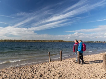 Aktivurlaub am Schladitzer See - CAMP DAVID Sport Resort in der Leipzig Region Ein Paar steht am Strand des Schladitzer Sees und schaut auf den See, Wasser, blauer Himmel